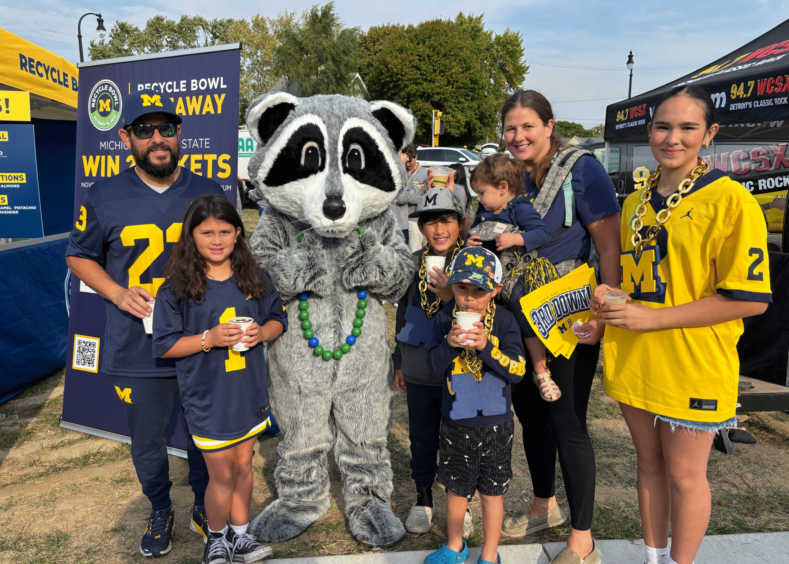 University of Michigan football fans pose with the Recycling Raccoon before the game, promoting PET bottle recycling and sustainability at Michigan Stadium.