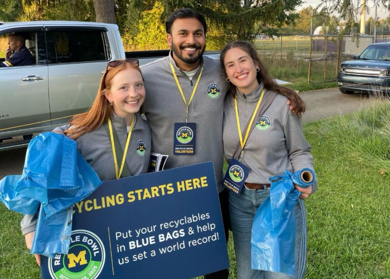 University of Michigan Recycle Bowl volunteers hold blue recycling bags and encourage fans to recycle PET bottles and other recyclables during game-day festivities.